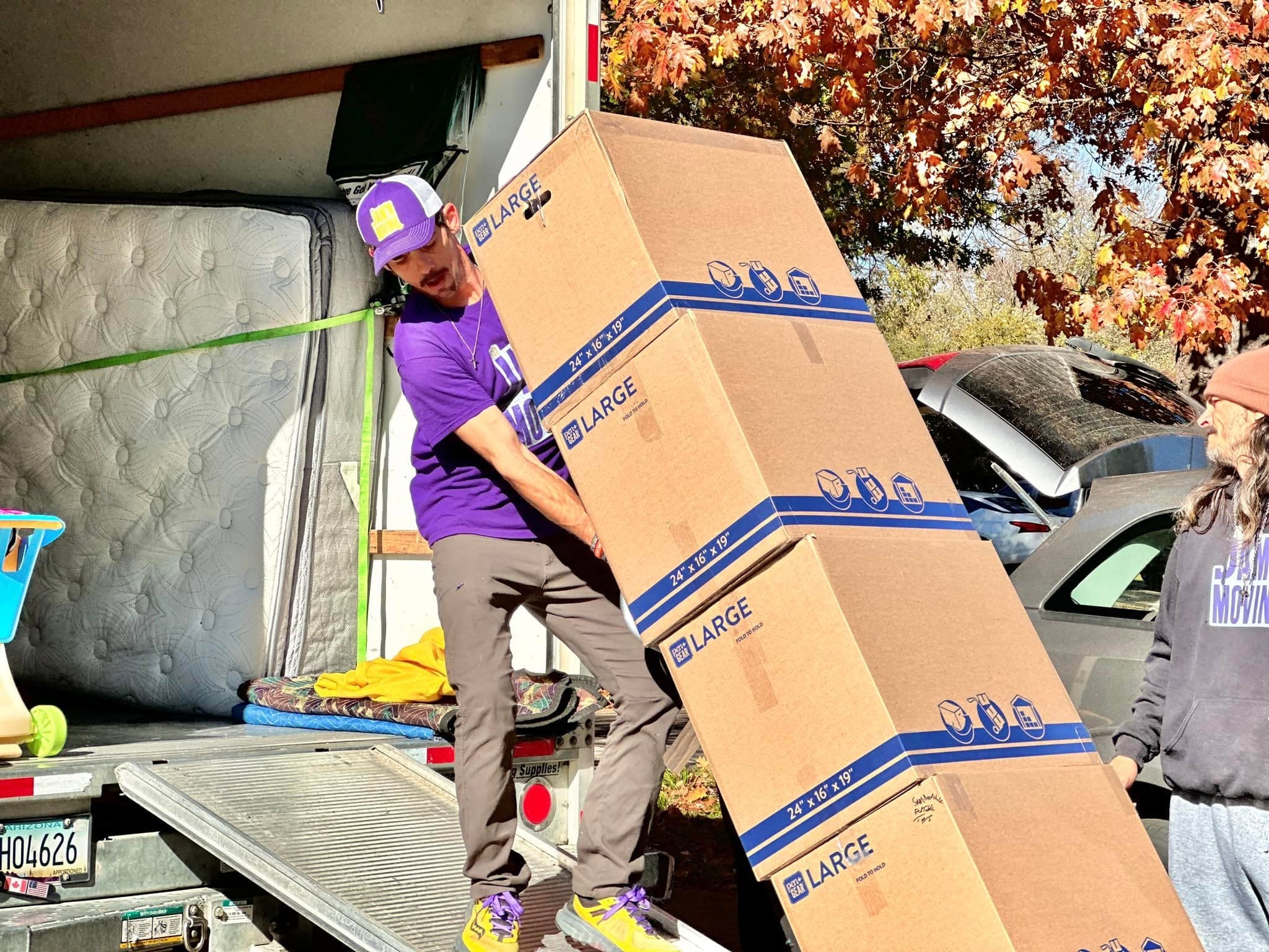 A Jam'N Moving crew member carrying a stack of boxes down the truck ramp
