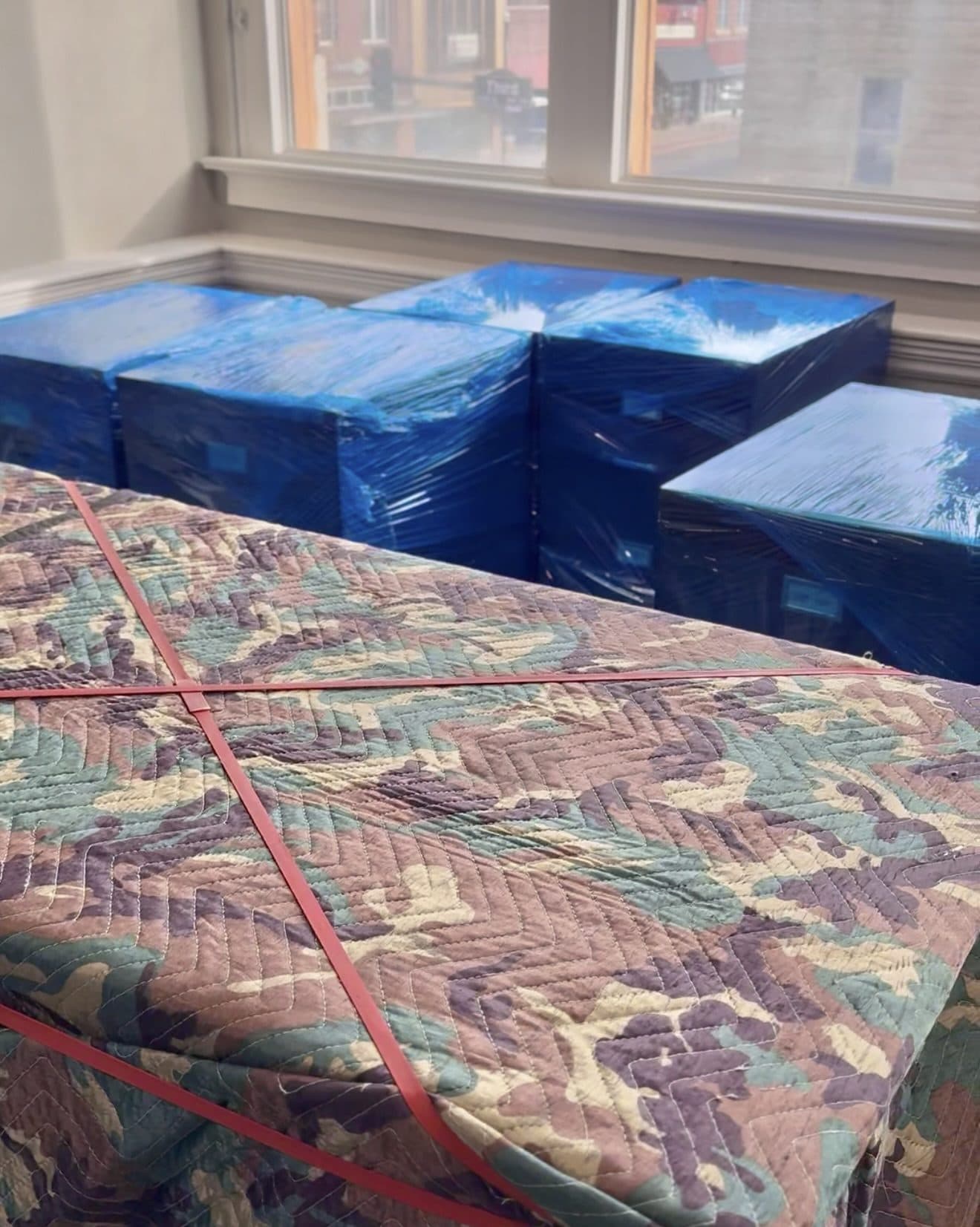 Office furniture shrink-wrapped and padded during a commercial move, with downtown Ponca City through the window
