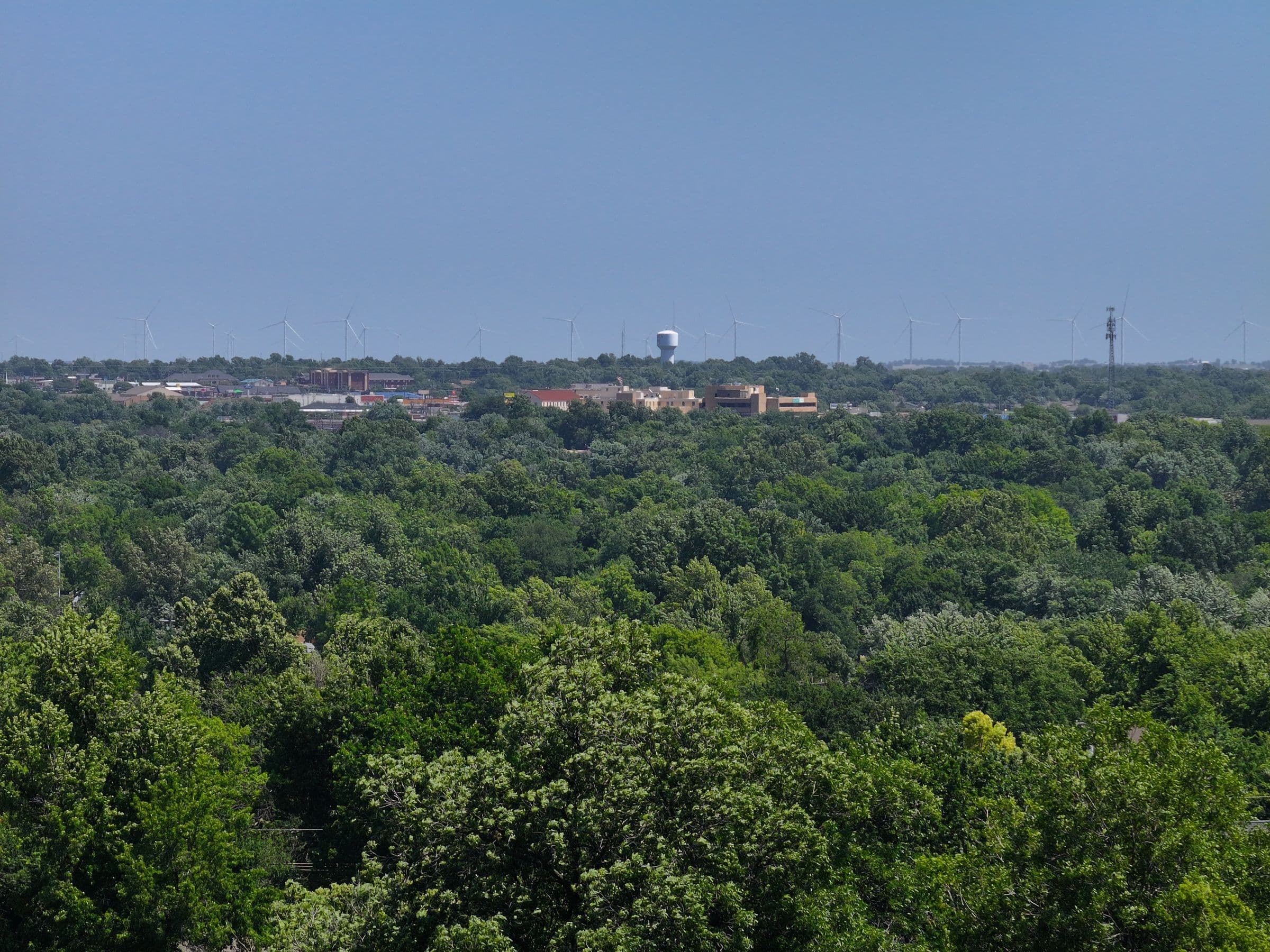 Ponca City seen across the treetops, with the water tower and wind turbines on the horizon